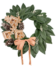 Decorative wreath with green leaves, gingerbread cookies, pinecones, and a brown ribbon on a white background.